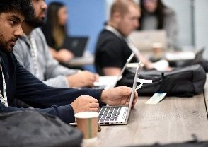 Graduates working on laptops around a shared table